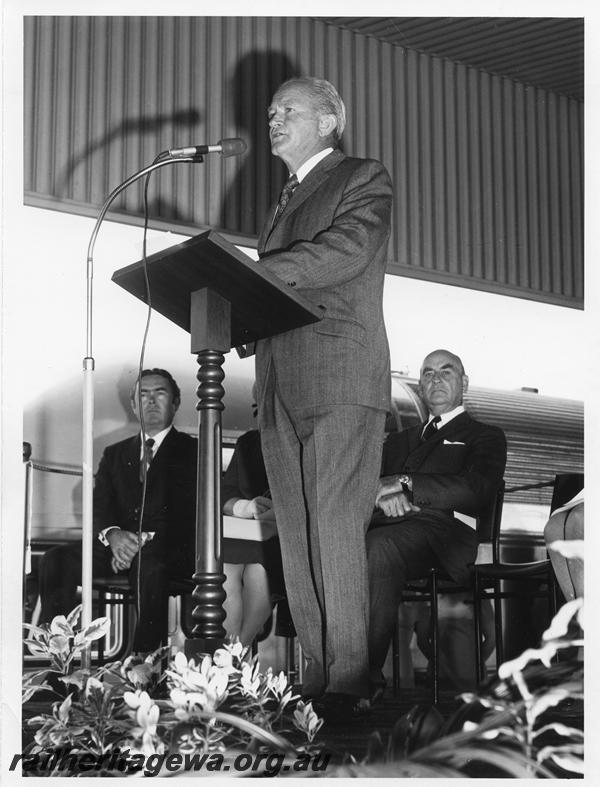 P00300
Ceremony for the launch of the Prospector railcar, East Perth Terminal, dignitary giving a speech, other official guests seated behind, the Premier, Mr J. Tonkin seated behind the speaker.
