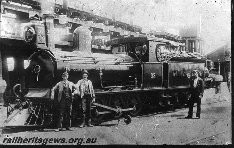 P02822
G class 32, 2-6-0 steam locomotive, in original condition,front and side view, elevated coal stage, water tower and shed in the background, workers standing in front of the loco, Kalgoorlie, EGR line, c1893-94. Same as p07414 & P07564
