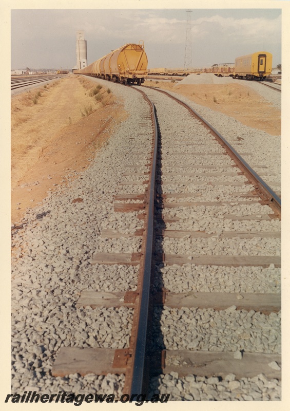 P03737
Track, rake of wheat hopper wagons, WBD Clss brake van, wheat silo, yard, West Merredin, EGR line, track level view
