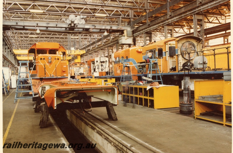 P03848
Fitting shop, block 3, Midland Workshops, Locomotive repair section, showing L class Westrail orange and TA shunter K class Westrail orange with blue chevron, R class Westrail orange with blue chevron. Ground level view along the workshop.
