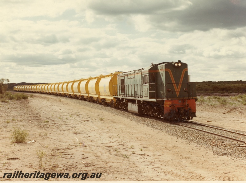 P03877
RA class 1915 diesel locomotive on mineral sands train, running short hood first, side and front view, in green with red and yellow stripe livery, XE class bogie ilmenite hoppers, en route to Eneabba.
