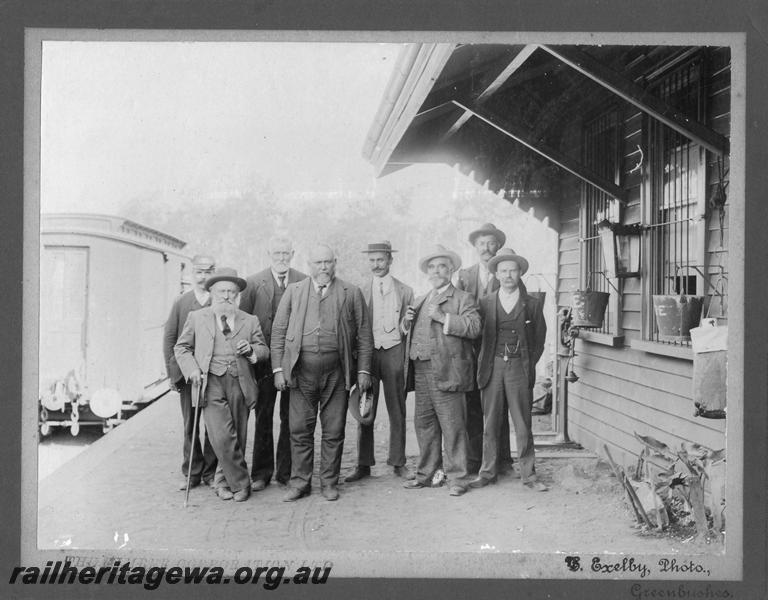 P10197
Group of men on a station platform, location possibly Greenbushes, PP line, The large gentleman in the centre of the group is Sir John Forrest, the station master, Mr F.S. Barnett is on the far left. A clerestory roofed brakevan is on the far left of the photo. The station building on the far right of the photo shows the platform scales, fire buckets and a water bag
