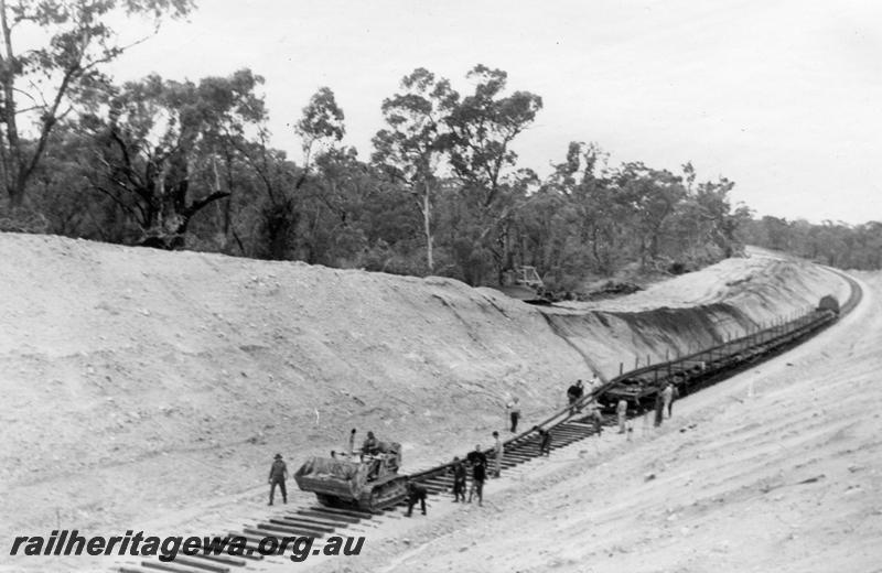 P12032
10 of 12 images of the construction of the Kwinana to Jarrahdale railway. (ref: The Railway Institute Magazine, July 1963).shows the caterpillar tractor hauling two rails from the wagons before being placed into position on the sleepers
