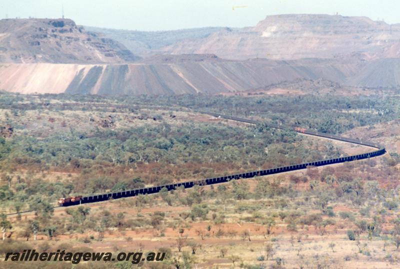 P12546
Newman, Port Hedland - Newman railway, BHP line, loaded train departing Mount Whaleback mine, two Alco units on the front, with 3 and the Locotrol car in the middle of the consist, waste dumps in the background

