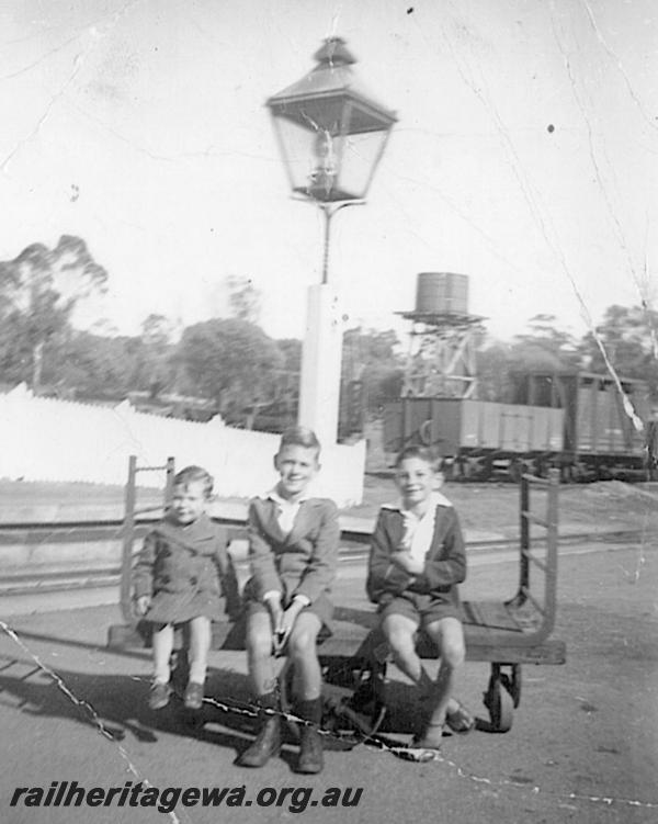 P12612
Platform trolley, station lamp, water tower, platform fencing, Clackline, ER line, three boys seating on the trolley
