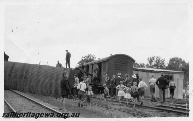 P13514
Derailed bogie van with a corrugated iron roof on its side, VA class van on adjacent track, onlookers, mainly children in attendance, date and location Unknown.
