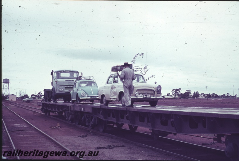 P15207
Motor vehicles being loaded onto Commonwealth Railways (CR) wagons, Parkeston, TAR line, water tower in the background
