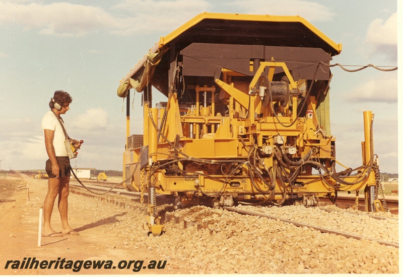 P15998
Mobile track maintenance machine, in yellow colour scheme, being operated by remote control, operator in tee shirt, shorts and thongs, near Dongara bridge, MR line, side and front view
