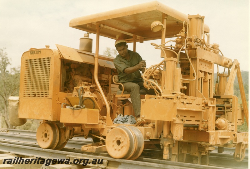 P16011
Motorised track construction trolley, number RRX104, in yellow colour scheme, operator driving, side and front view

