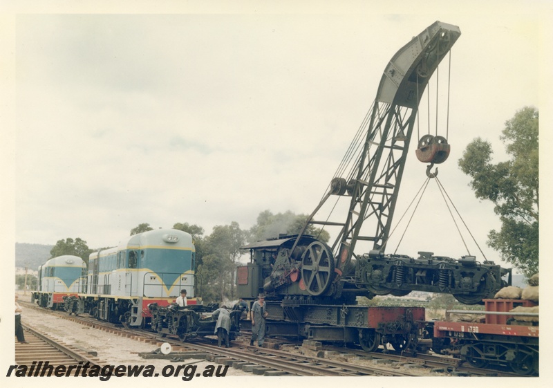 P16022
Breakdown crane no 23, lifting bogie, two diesel locos in light blue with dark blue and yellow stripe livery, bogie on tracks, portion of U class 1730 wagon, view from track level
