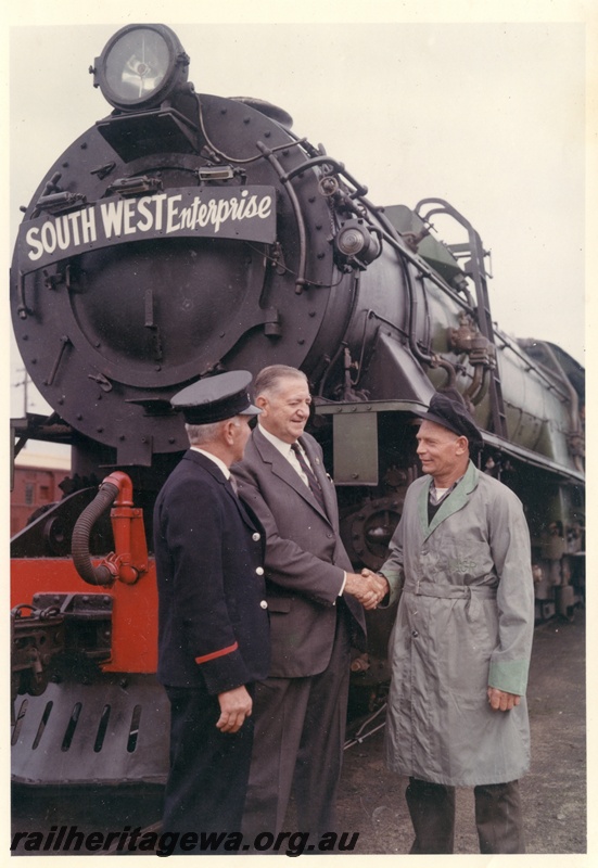 P16060
Commissioner of Railways, Mr. C. G. C. Wayne shaking hands with the driver while a porter watches on. The front of the V class locomotive is adorned with the 