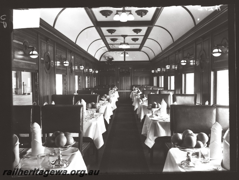 P16182
Commonwealth Railways (CR), dining car, tables set with bowls of fruit prominent, fan, interior view
