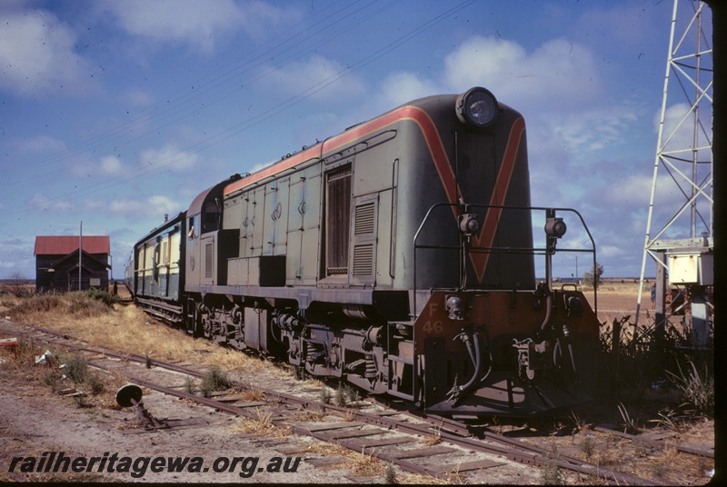 P16678
F class 46 in green with red and yellow stripe, on passenger train, standing at small country station, station building, point lever, aerial tower, side and front view
