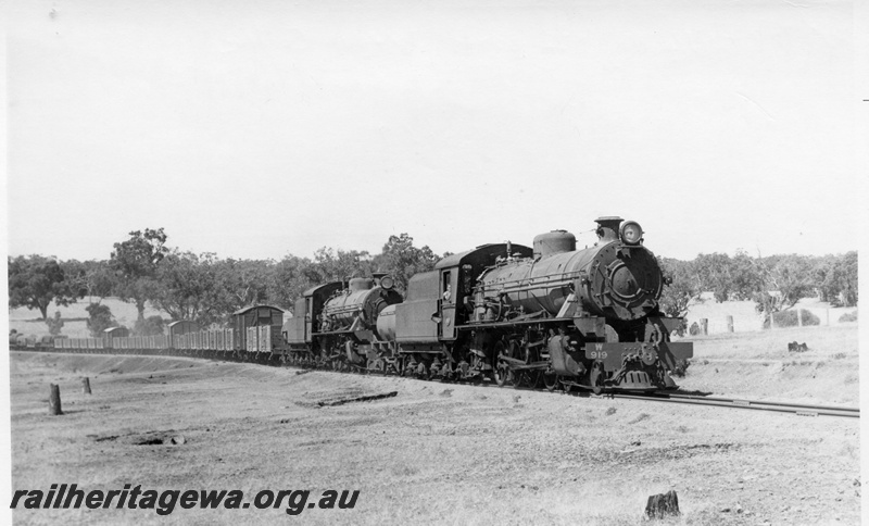 P17375
W class 919 & 914 steam locomotives at the head of 54 Goods between Wagin and Collie. Front & side view of front locomotive. Both locomotives have water tankers behind their tenders. BN line.
