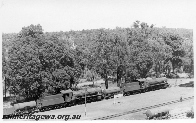 P17382
W class 919 & W class 914 steam locomotives arriving Bowelling with 104 Goods from Wagin. WB line. The line in foreground is the Collie - Narrogin line. Siding nameboard between rail lines and a water tanker on the adjacent goods road.

