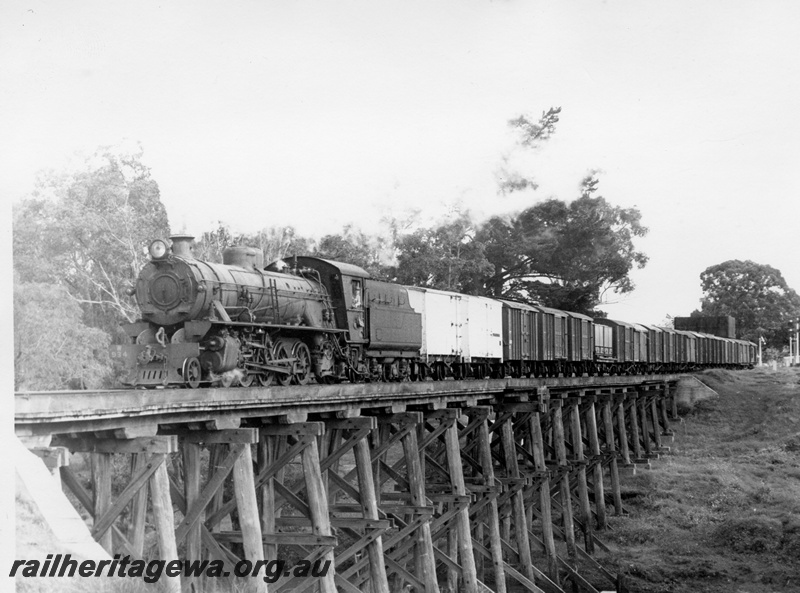 P17464
W class 934 steam locomotive hauling a goods train over the Preston River bridge at Boyanup enroute to Bunbury. PP line. Note the semaphore signals and station building in background.
