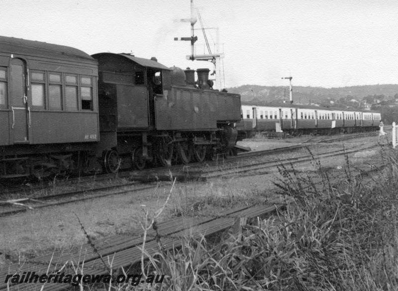 P17634
An unidentified D class locomotive at the head of a suburban train. Location Unknown. Note portion of AY class 452 carriage behind the loco and 4 car suburban railcar set to the front of locomotive. Bracket signal at left front of locomotive.
