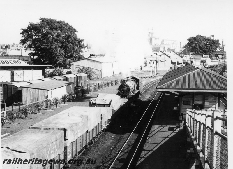 P17653
W class 922 steam locomotive shunting at East Perth. ER line. All wagons attached to locomotive have their loads covered by tarpaulins. Varied covered wagons in siding to left. Ramp from overhead footbridge going down to booking office.
