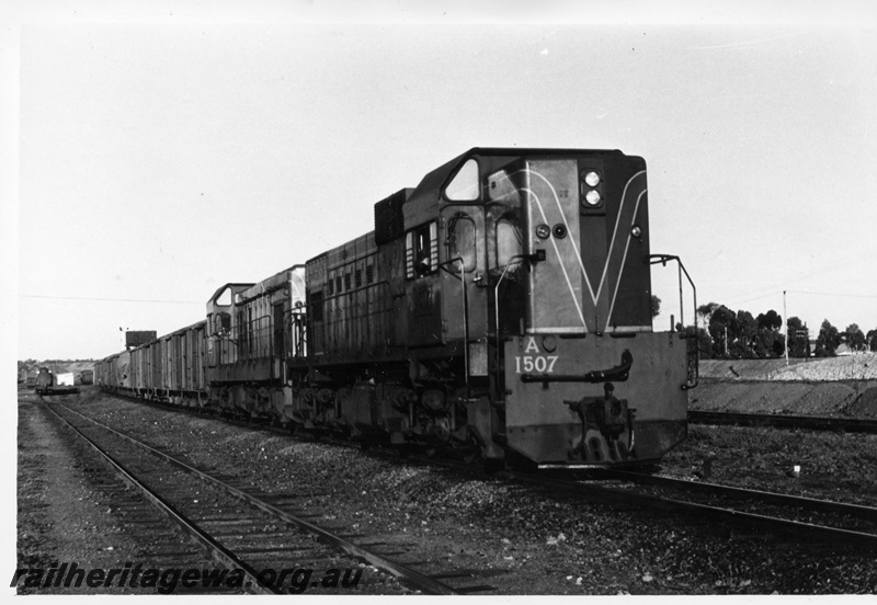 P17735
A class 1507 diesel locomotive in green with red and yellow stripe livery and an unidentified A class hauling a goods train. Location Unknown.
