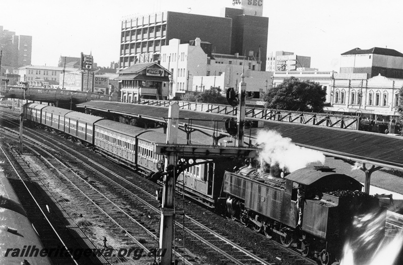 P17736
DD class 598 steam locomotive arriving at City Station with a suburban service. Note the semaphore signals in the foreground. Former SEC building in background. signal box and Barrack Street overhead bridge in view. Note the roofed area of the platform. ER line.
