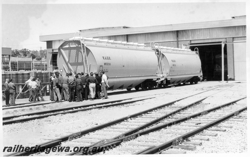 P17846
WW class 32018 standard gauge wheat hopper with an unidentified wagon at the maintenance depot at Avon Yard. Westinghouse brake training session in progress. Adjacent to the attentive workers is the oil supply storage area.
