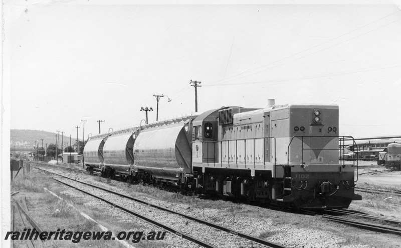 P17848
J class 102 diesel locomotive with 3 WWA wheat hopper wagons at Midland near the western end of the Workshops. To the right is an unidentified K class and B class locomotives. Note yard light tower above the middle wheat hopper.
