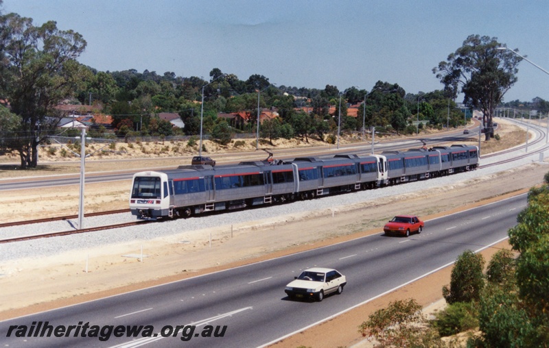 P17951
AEA class EMU railcar set with the red stripe above the windows, comprising two 2 car sets, road in foreground, near Garnkirk Road, Greenwood, Northern Suburbs line, front and side view
