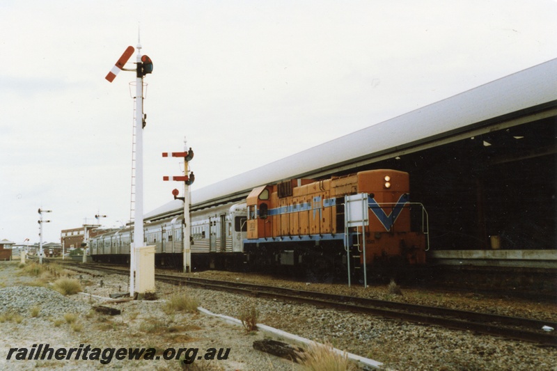 P18024
A class 1511, on train of stainless steel cars, arriving at station, signal box, pedestrian overpass, wool stores building, signal, bracket signals, Fremantle, ER line
