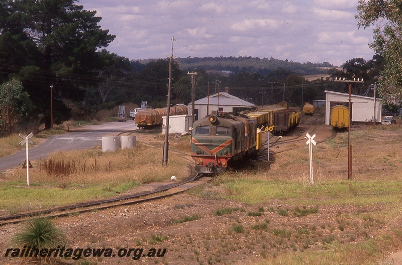 P19727
XB class 1027 on goods train departing station, rakes of goods wagons, station buildings, goods shed, sidings, crossing, Boyup Brook, DK line

