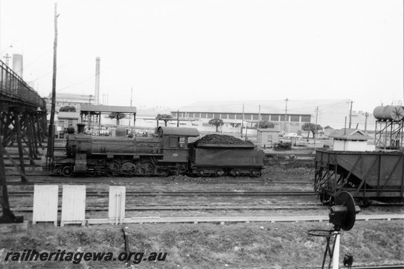 P21113
F class loco, light signal, wagon (part), pedestrian overpass, power station, industrial buildings, trackside buildings, fuel tanks, East Perth running sheds, ER line, side view 
