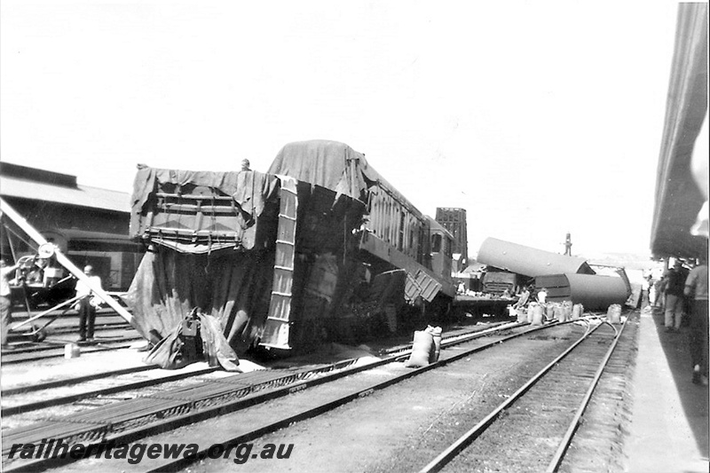 P23013
Derailment at Northam 1 of 3, diesel loco off tracks, carriages on sides and askew, station platform and canopy, tracks, onlookers, Northam, ER line, track level view 
