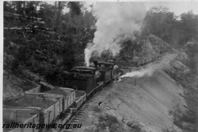 P02008
A pair of G class locos hauling a rake of side tipping wagons on the construction of the Denmark to Nornalup railway, D line, elevated view for the rear of the train looking towards the locos, c1928/29
