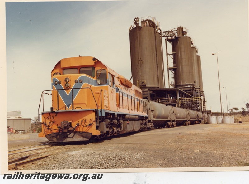 P04148
2 of 3, L class 273 standard gauge diesel in Westrail orange livery, front and side view, on nickel train of WNA class nickel ore wagons being loaded, Red Mine Kambalda.
