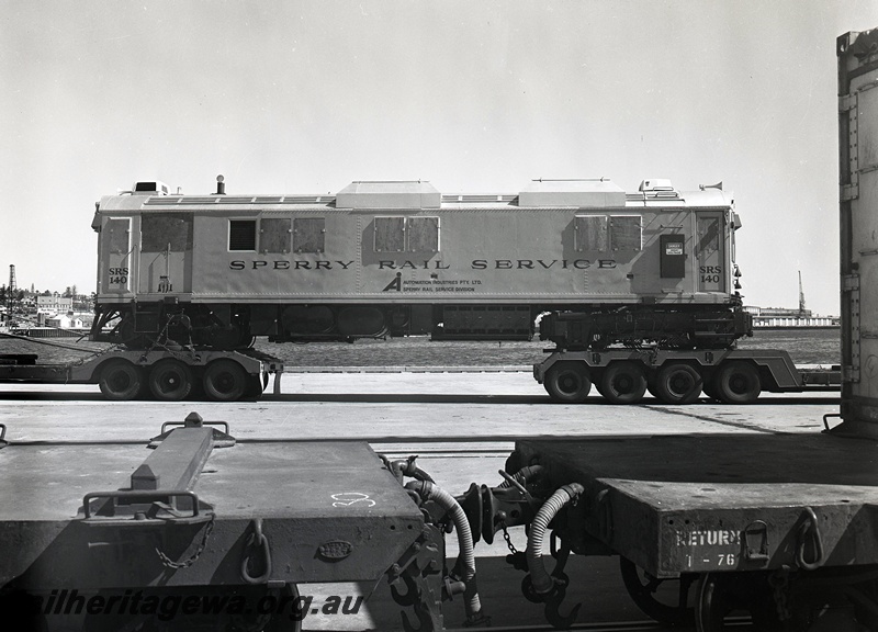P15051
Sperry Rail Service railcar 140, on road transport trailer, in middle distance, side view, in foreground the coupling mechanism between a flat top wagon with WAGR plate and 