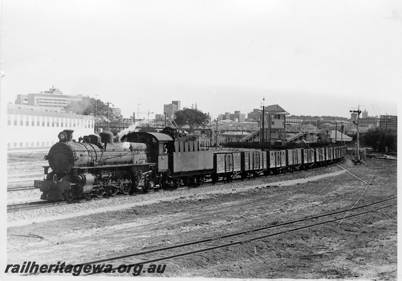 P17769
PMR class 732 steam locomotive departing East Perth on 35 Goods. Semaphore signal to right of train. Signal box towering over train in mid background. Rail track in foreground is remains of line to Power House. Royal Perth Hospital to left background.
