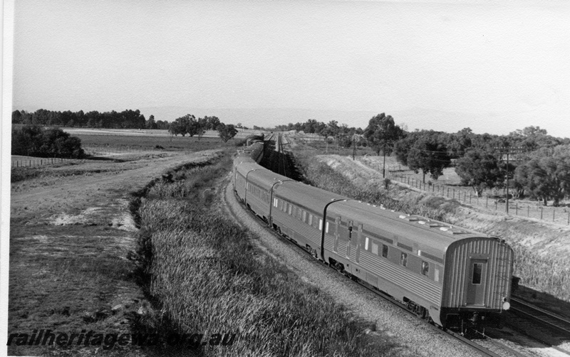 P17777
Train comprising stainless steel passenger carriages, passing through rural countryside, moving away from camera, rear and side view, c1969
