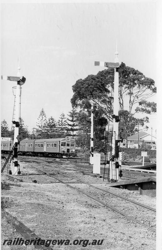 P17814
An unidentified 4 car ADK/ADB railcar set on a Perth bound suburban service departing Claremont. ER line. Note the semaphore signal sets, electrical boxes, end of platforms and trackage in the foreground. 

