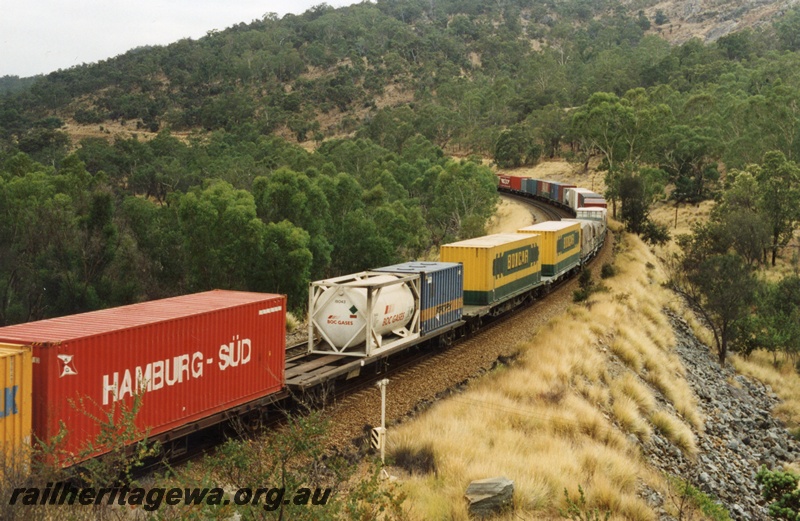 P18008
Part of the consist on Sydney to Perth freight train, on a bend on an embankment through hills, AN class 9 and GM class 38 not visible, view from elevated position
