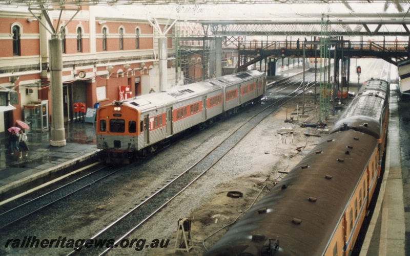 P18067
10 of 11 Construction of new Perth City station, DMU, orange and stainless steel, arriving on platform 4 from Fremantle, DMU standing at another platform, orange livery with blue stripe, roof supports, pedestrian overpass, light signals, Perth City station
