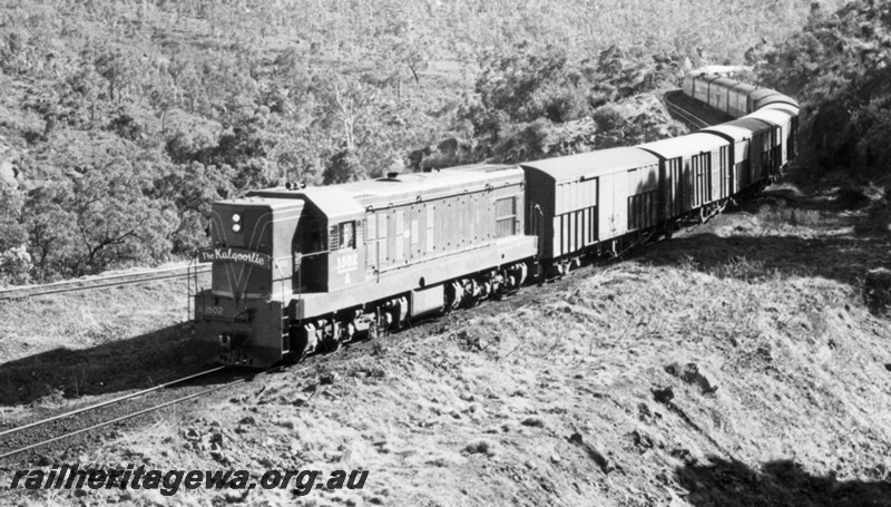 P18110
A class 1502 diesel locomotive hauling The Kalgoorlie at Tunnel Junction approaching the tunnel. ER line. Bogie covered vans between locomotive and carriages.
