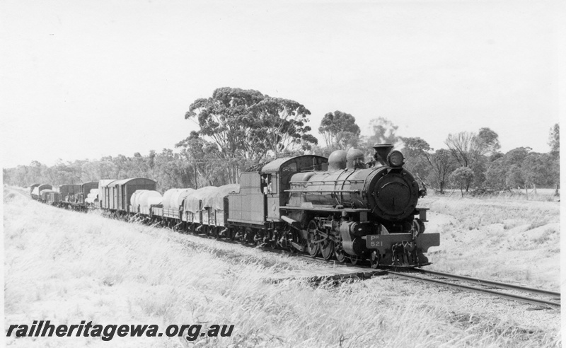 P18113
PR class 521 steam locomotive hauling 17 goods between Brookton and Pingelly. GSR line. Front view of locomotive and side view of locomotive and train.
