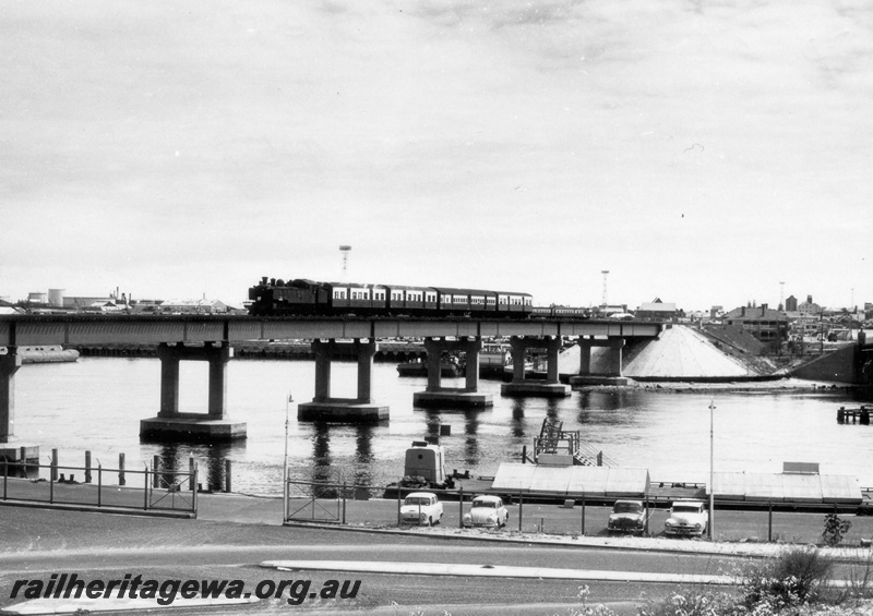P18114
An unidentified DD class steam locomotive on a Fremantle bound suburban train crossing over the Swan River via the Fremantle railway bridge. ER line. Limited water traffic on river. 
