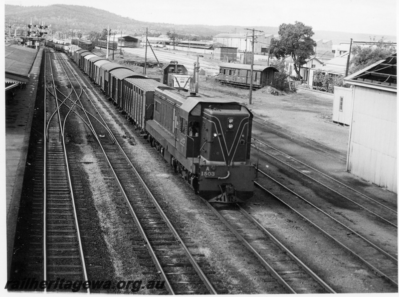 P18115
A class 1503 diesel locomotive hauling a goods train through Midland Station enroute to Fremantle. ER line. Part of station canopy and semaphore signals to left, B class diesel hydraulic shunting locomotive in background with a written off Z type brakevan up against the dead end.
