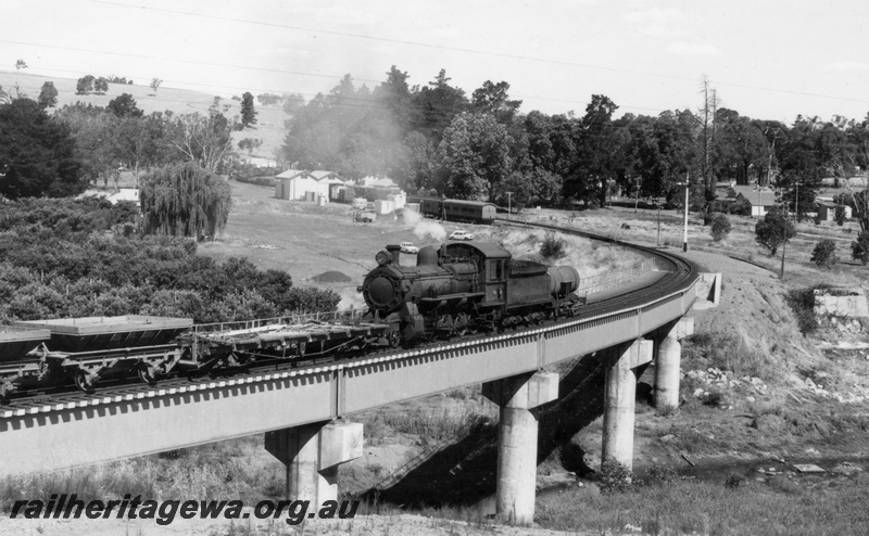 P18220
FS class 423 steam locomotive, front and side view, on ballast train, crossing concrete bridge, running tender first with J class tanker leading, station buildings, goods shed, rolling stock, semaphore signals, LA class hoppers, Balingup, PP line.
