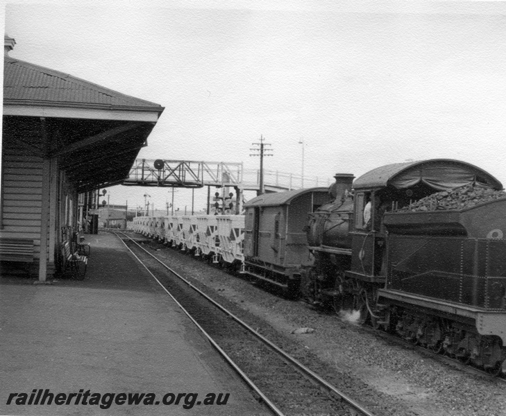 P18345
4 of 4, Rake of WMC class hoppers, F class 412, shunting hoppers and brakevan, station building and platform, signal, light signals, overhead footway, end and side view
