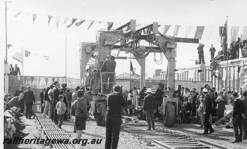 P18480
11 of 12 images relating to the ceremony for the linking of the standard gauge railways at Kalgoorlie, last 30 foot section of track linking the standard gauge railways is laid, track laying machine, seated guests and spectators look on

