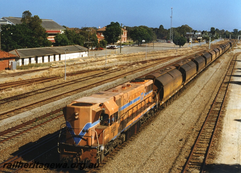 P18653
D class 1561 heading an empty mineral sands train of XE class hopper wagons to Chandalla, on the Midland Railway line, passing through Midland. The white building to the left of the locomotive is the former workshop workers bicycle shed.
