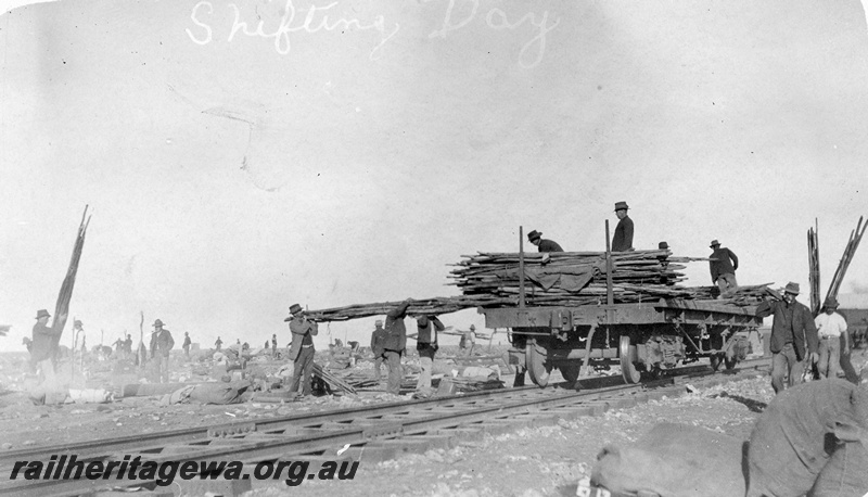 P19167
Shifting day for Commonwealth Railways (CR) construction camp, flat wagon being loaded with timber, workers, bags, swags, TAR line
