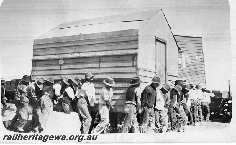 P19168
Moving Commonwealth Railways (CR) construction camp, workers carrying wooden buildings, buildings being loaded on to wagons, TAR line
