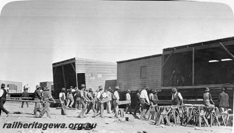 P19175
Commonwealth Railways (CR) camp being loaded onto flat wagons, buildings, trestles, workers, TAR line
